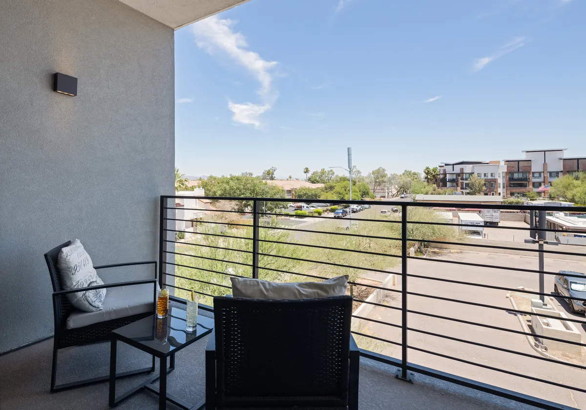 A serene private balcony with comfortable outdoor furniture, offering a scenic view of the landscape and blue sky. The space is perfect for enjoying morning coffee or evening conversation, blending indoor comfort with outdoor energy.