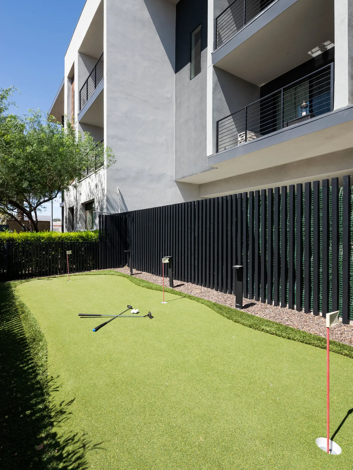 A well-maintained artificial putting green bordered by modern architecture, with golf clubs set up for play. The scene conveys a playful yet sophisticated outdoor recreational amenity for guests to enjoy casual competition and relaxation.