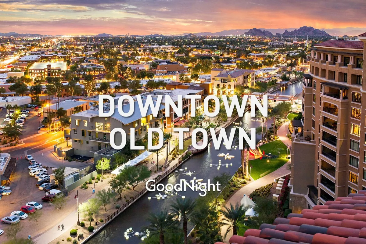 A stunning evening view of city lights sparkling along a water canal, with mountains silhouetted in the background. The scene captures the lively yet intimate energy of Scottsdale at dusk, hinting at vibrant nightlife, romantic dinners, and memorable strolls.