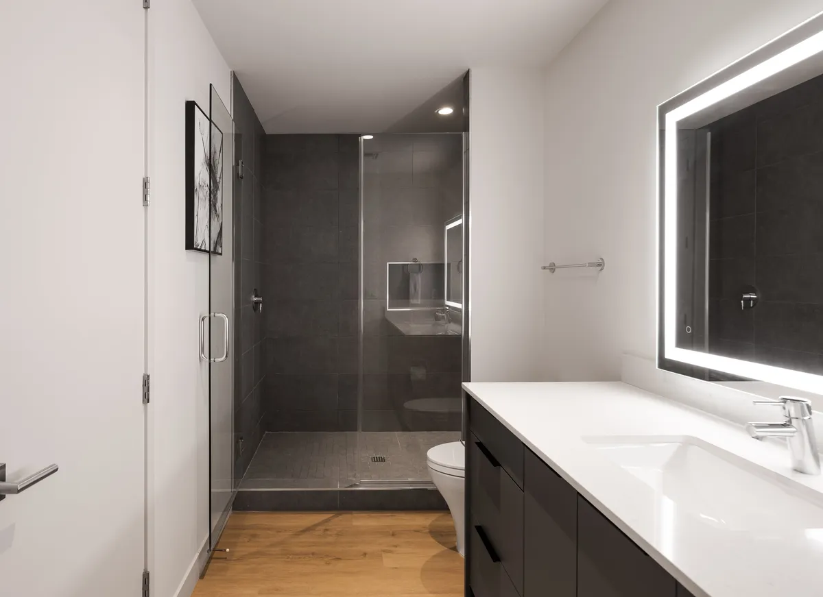 A modern ensuite bathroom featuring a walk-in shower, vanity, and backlit mirror. The space feels fresh, spa-like, and tailored for comfort and relaxation.