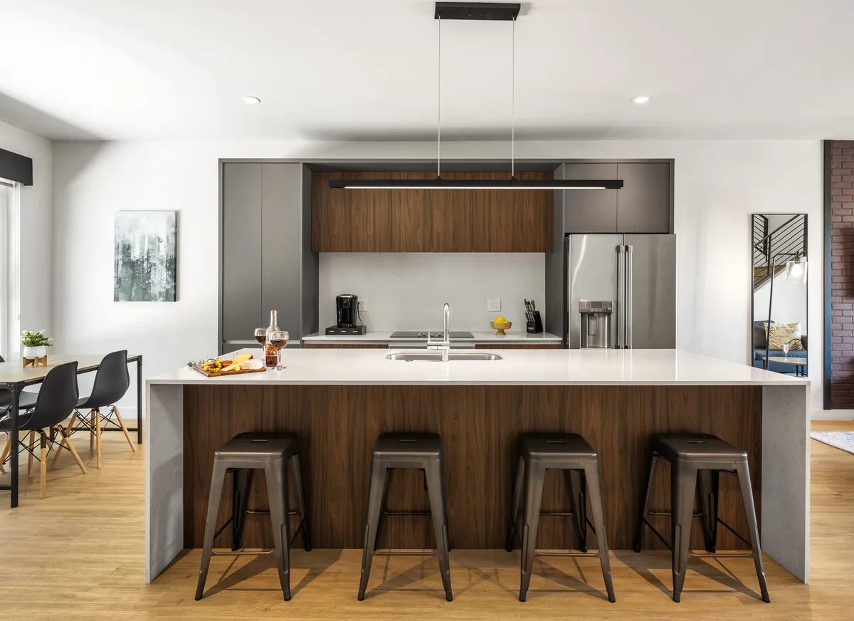 A bright, open kitchen featuring a spacious island with stylish stools, modern appliances, including a prominent range, and tasteful wall art. The setting is designed for both cooking and socializing, with the island serving as a central gathering spot.