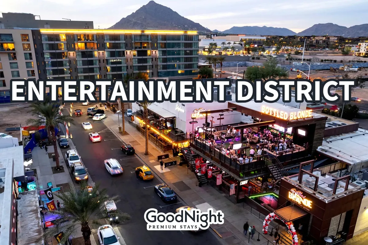 A nighttime scene showcasing the entertainment district signage, the prominent Bottled Blonde venue, cars lining the street, and mountains in the background. The street is alive with the energy of nightlife, dining, and live music, with groups of friends and couples headed to venues.