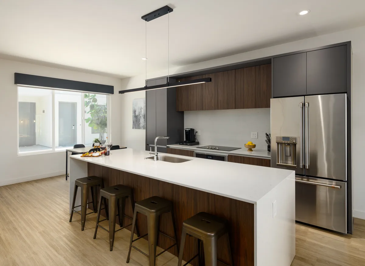 A contemporary kitchen with an island countertop, modern appliances, inviting stools, and a large window providing ample daylight. The space is ideal for both cooking and social gatherings, with functional and attractive design.